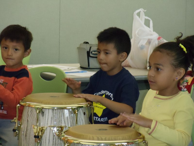 Three children playing drums in a classroom