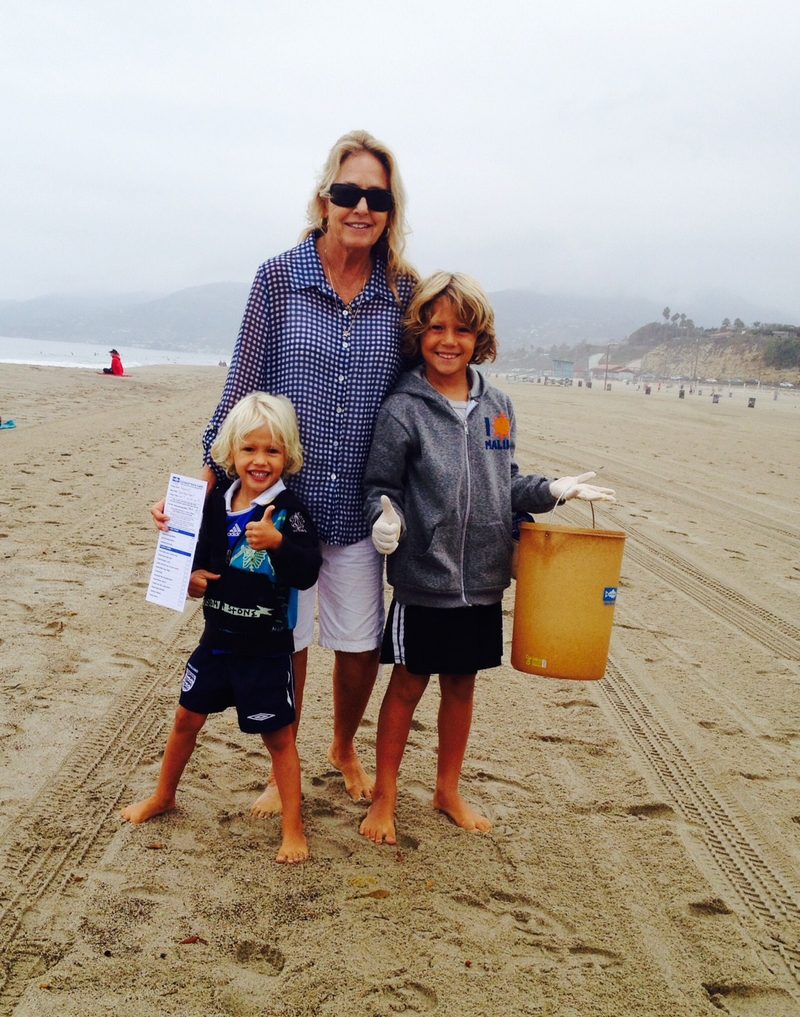 An adult and two children on a wide beach carrying a bucket of collected litter