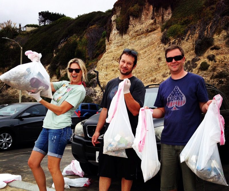Three volunteers holding up bags of collected litter beside a car park