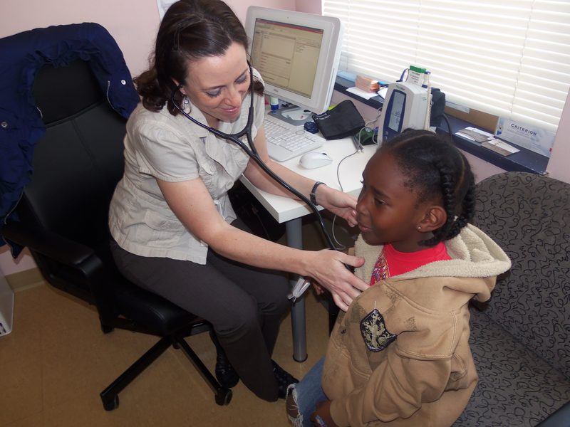 A health worker with a stethoscope examining a child at a desk
