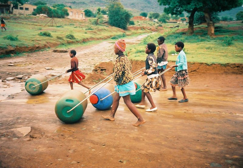 Children rolling water containers along a dirt road
